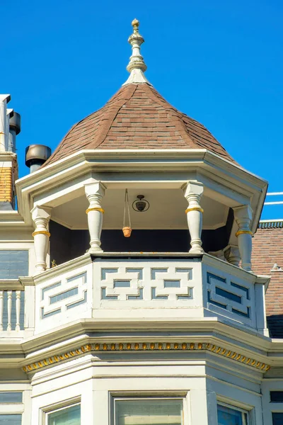 stock image House spire or turret with metal tip and white balcony with accent paint and wooden pannels in midday sun with blue sky. In the neighborhood or in the city downtown or in a suburban area.