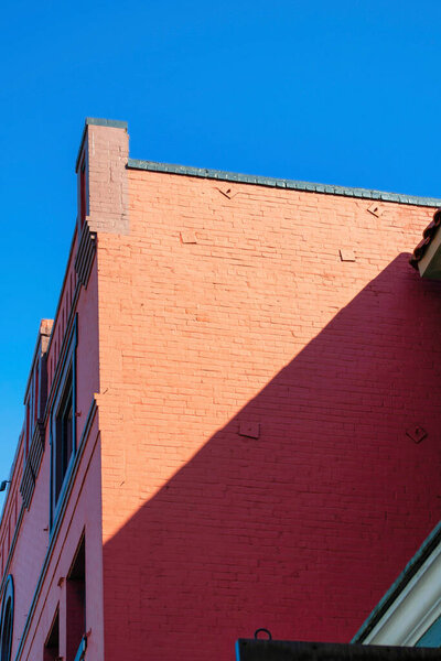 Red brick building facade on sunny surface of structure with shade streak in blue sky background in urban part of the city. In the neighborhood on apartment building or business structure.