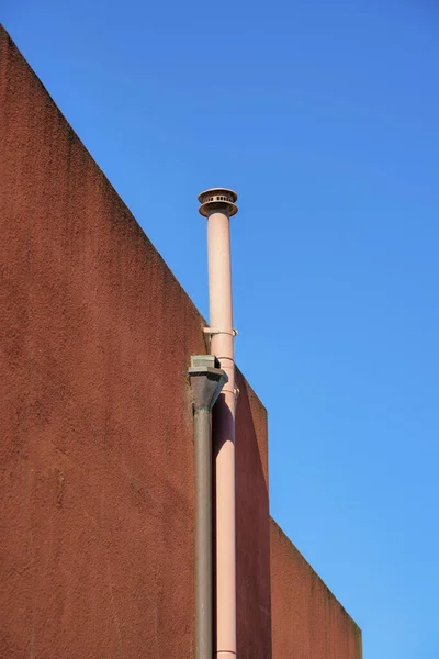 Red stucco building exterior with visible sunlit metal chimney pipe with clear blue sky background in late afternoon sun midday. In the neighborhood or in the suburban or urban part of the city.