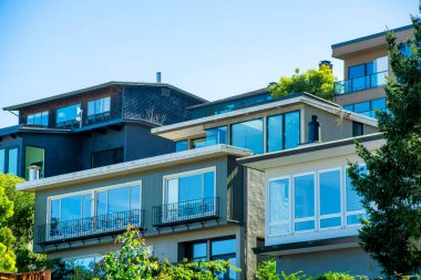 San Francisco 'nun tarihi bölgelerindeki modern evler. Şehir merkezinin gölgesinde, sıva evlerinin görünür pencereleri var. Mahallede mavi gökyüzü arka planlı ön bahçe ağaçları var..