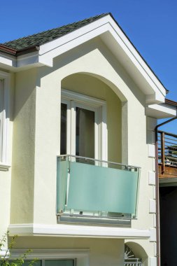 Temiz dekoratif balkonlu, beyaz çatılı ön cephe boyalı ve evin dış cephesinde koyu çatı kiremitleri olan beyaz sıva evi. Banliyöde güvenli bir şehir caddesinde güneş gören bir mahalle..