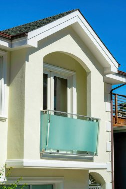 Temiz dekoratif balkonlu, beyaz çatılı ön cephe boyalı ve evin dış cephesinde koyu çatı kiremitleri olan beyaz sıva evi. Banliyöde güvenli bir şehir caddesinde güneş gören bir mahalle..