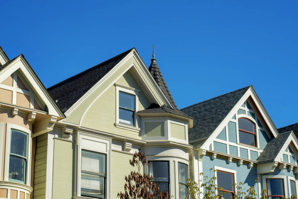 Row of historic houses in San Francisco California with front yard trees and clear blue sky background with beige and blue color. In the city or in the downtown neighborhood in midday sun.