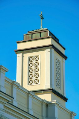 Beyaz ve bej kaplamalı Chruch çan kulesi. Düz çatının üstünde haç olan açık mavi gökyüzü arkaplanı var. Şehrin kentsel kesiminde ibadet yeri olarak kullanılıyor..