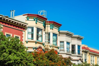 San Francisco 'nun şehir merkezindeki tarihi evler. Öğleden sonra güneşli, açık mavi gökyüzü arka planlı. Bej ve kahverengi renkli görünen dekoratif cepheler ve pencereler.