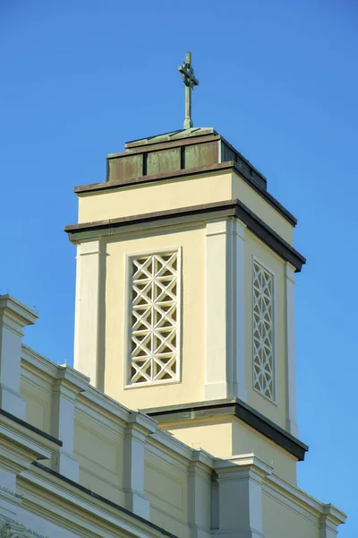 带有米色和白色粉刷的灌木尖塔 蓝天背景清晰 顶部有交叉的平面屋顶 在城区附近的宗教礼拜场所 — 图库照片