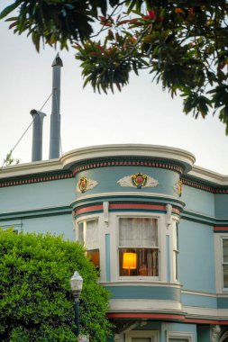 Görünür ışık ve düz çatılı, beyaz aksanlı dış görünüşlü ve mahalledeki ön bahçe ağaçlarıyla çevrili gizli bir apartman penceresi. Şehir merkezinde sisli bir günde öğleden sonra.