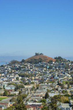 San Francisco 'nun merkezindeki kırsal bir tepede. Kenar mahallelerde mavi-beyaz gökyüzü var. Evler, evler ve binalar. Gün ortasında ön bahçesinde ağaçlar var..