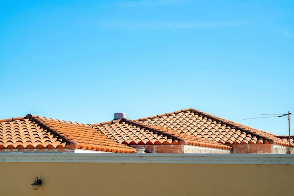 Row of adobe red roofs with tiles and a wall in the foreground with gradient blue and white sky background in midday sun. In the neighborhood or in the suburban area of the downtown city no clouds.