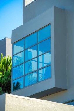 Dekoratif modern pencere, on iki ayrı cam pencere ve ön bahçe ağaçları ve mavi-beyaz gökyüzü desenli ızgara desenli. Ev ya da ev çimento ve güneşli istinat duvarlı blok tasarımı.