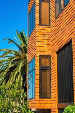 Turuncu ve kırmızı ahşap dış yüzeyi bina, ev ya da evin görünür pencereleri ve mavi gökyüzü olan ön bahçeli palmiye ağaçları. Gayrimenkul ve ev almak için banliyö mahallesinde.