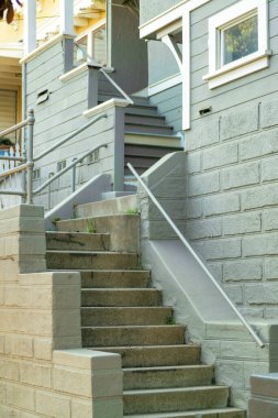 San Francisco 'nun banliyösündeki konutun önünde gün ortasında ya da öğleden sonra gölgede uzun merdivenler var. Turuncu ve yeşil tuğlalı duvar. Evde veya evde tırabzan ve beyaz süslemeler var..