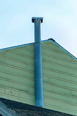 Gri metal baca borusu bej ya da beyaz yatay olarak kesilmiş ahşap ya da ahşap çerçeveli ev gölgede öğleden sonra. Mavi beyaz bulutlu gökyüzü olan modern bir ev..