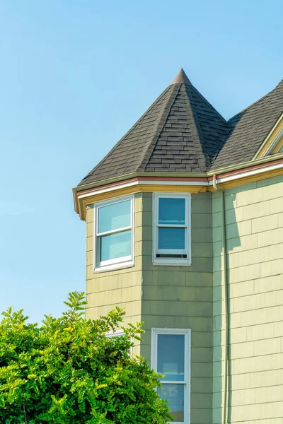 stock image Housing turret or spire on side of home with beige horizontally wood slatted house with windows with white trim on gray tile roof. Late afternoon sun with blue and white sky in suburban neighborhood.