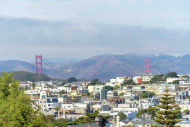 Bulutlu banliyöler ve San Francisco California 'da şehir merkezindeki Golden Gate Köprüsü yakınlarında bulutlu bir geçmişi var. Gün ortasında, banliyölerdeki evler ve binalar sisli..