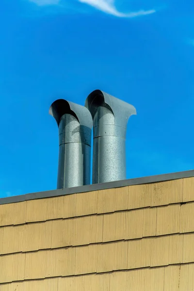 Metal air vents or chimneys with wooden horizontal pannels with beige color and blue sky with slight whispy clouds. In midday sun on modern building or house in the city or neighborhood.