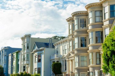 San Francisco California 'da ön bahçesi ağaç ve mavi gökyüzü olan renkli ve dekoratif evler. Öğleden sonra güneş batarken bazı bulutlar bu civarda pahalı konutlarda.