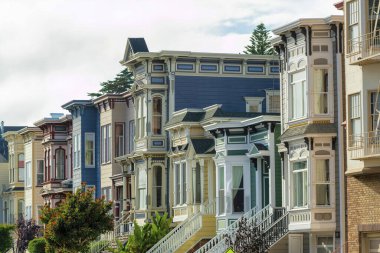 San Francisco 'nun modern kesiminde mavi, pembe ve kırmızı evleri olan renkli evler. Arka planda ve ön bahçede bulutlu ya da sisli gökyüzü ile öğleden sonra gölgesinde.