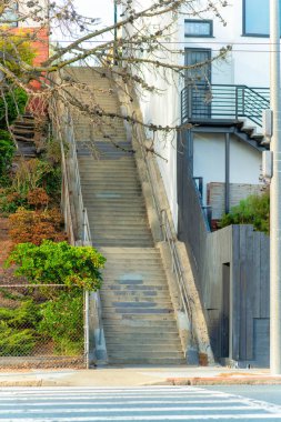 Çimento basamakları olan büyük endüstriyel merdivenler yan taraflarında ağaçlar ve binalar olan gri metal el rayları. Akşam güneşinde şehrin gölgesinde ya da şehir merkezinde.
