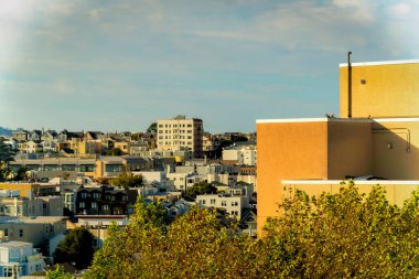 Ağaçlar ve banliyö evinin arka planıyla çevrili bej ve kahverengi kaplamalı kentsel alan. Öğleden sonra güneşinde şehir merkezinde gri ve sisli bir gökyüzü.