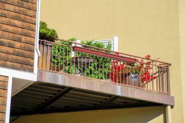 Köşedeki kama, mahalledeki balkon ve terasta ya da evin yan tarafındaki banliyö ortamında parçalanmış. Balkonda sıva duvarlı bitkiler ve şehir merkezindeki binada ahşap panellerle..