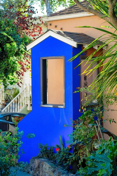 Blue exterior paint on mini house facade near front door entrance in yard on patio. In late afternoon shade with trees and foliage in the neighborhood on a house or home facade midday.