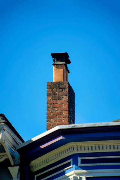 近所に装飾的な青のファサードとフラット屋根とモダンな家の上に金属パイプと赤レンガの煙突 冬の日に火事を起こしたり屋根の上で煙を出したり — ストック写真
