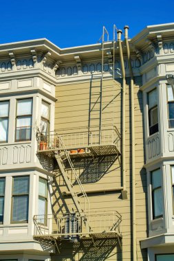 Kahverengi ahşap kaplama bina metal yangın merdiveni ve düz çatılı balkon ve öğle güneşinde dekoratif cephe. Şehrin kentsel kesimlerinde ya da apartmanlarında.