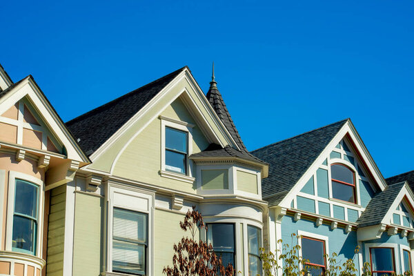 Row of historic houses in San Francisco California with front yard trees and clear blue sky background with beige and blue color. In the city or in the downtown neighborhood in midday sun.