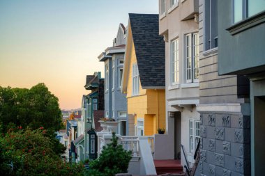 San Francisco California 'da şehir merkezindeki şehir merkezindeki modern evlerde günbatımında ön bahçe ağaçlarıyla aydınlanıyor. Okyanusta turuncu ve gri cepheli şehirlerde ya da mahallelerde.