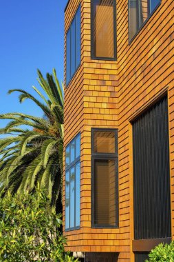 Turuncu ve kırmızı ahşap dış yüzeyi bina, ev ya da evin görünür pencereleri ve mavi gökyüzü olan ön bahçeli palmiye ağaçları. Gayrimenkul ve ev almak için banliyö mahallesinde.