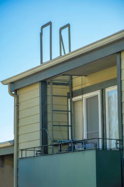 Şehir merkezindeki bir ev ya da evde çatısı olan güvenli bir yangın merdiveni var. Mavi ve beyaz gökyüzü, balkonda metal basamaklar saklı..