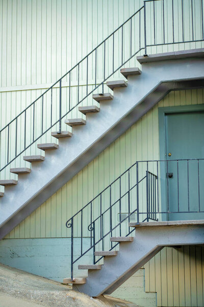 Dual metal old schools tyle staircases on side of building the urban downtown city of historic districts in suburban neighborhood. Beige stucco exterior with cement steps and hand rails on structure.