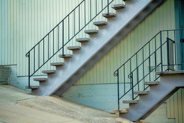 Top and bottom stair case with metal hand rails and cement steps on slanted street on side of beige stucco building in urban city. In late afternoon shade in the downtown suburban neighborhood.