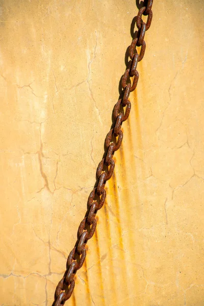 Orange yellow stone background with cement and rusty chain hanging across the urban exterior of building or structure downtown. In midday or late afternoon sun with dripping rust stains in city.