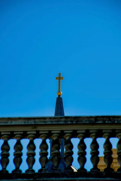 Forced perspective with cross atop church steeple against cement balcony on patio in a church courtyard and garden. Silhouette of balcony and cross in distance with dark blue sky background.
