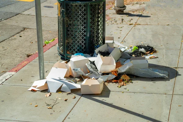Pile of generic trash in the run down inner cities and downtown areas of american decline in infrastructure with garbage and debris near can. Visible road sign and sidewalk in afternoon sun in city.