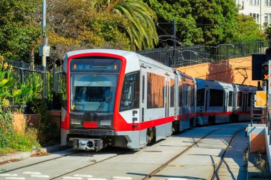 Tramvay ya da tren raylı kırmızı ve gri boyalı arka planda çalılar ve ağaçlarla şehir merkezindeki bir yerde. Ulaşım ve toplu taşıma için San Francisco 'da Kaliforniya.