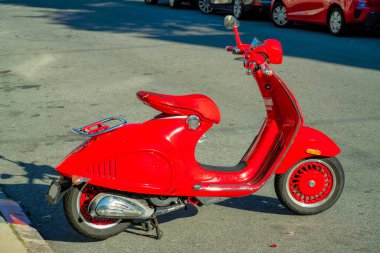 Kırmızı motosiklet ya da elektrikli bataryalı scooter ve şehir merkezinde taşıma için tekmeleme standı olan siyah lastikler. Günün ilerleyen saatlerinde araba ve arka planda gölgeli park yeri..
