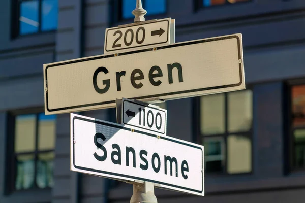 White and black road sign that says sansome and green with dense urban background in shade and sun midday. In the city for cars and transportations for busses traveling in the neighborhoods.