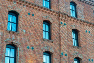 Non descript brick building with visible blue glass windows in afternoon shade in the business districts downtown. In the urban part of the neighborhood on business or factory.