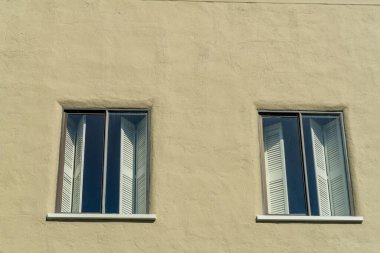 Beige or brown stucco building with two visible glass windows with shutters or curtains on side of structure. Used for design or texture purposes in the urban part of downtown neighborhoods.