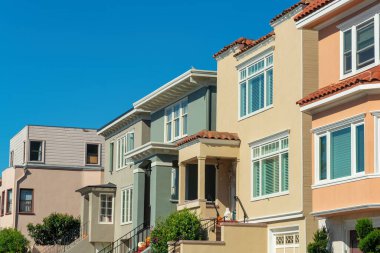 Row of decorative and colorful house facades or exteriors on homes in historic district of san francisco california. Afternoon sun with blue sky in middle class suburban american dream neighborhood.