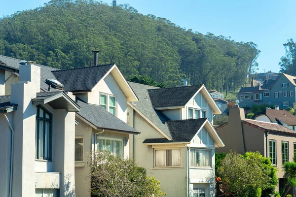 Row of white and beige stucco house with visible windows and chimneys with forest background and clear blue sky. In afternoon in suburban part of san francisco downtown city neighborhoods.