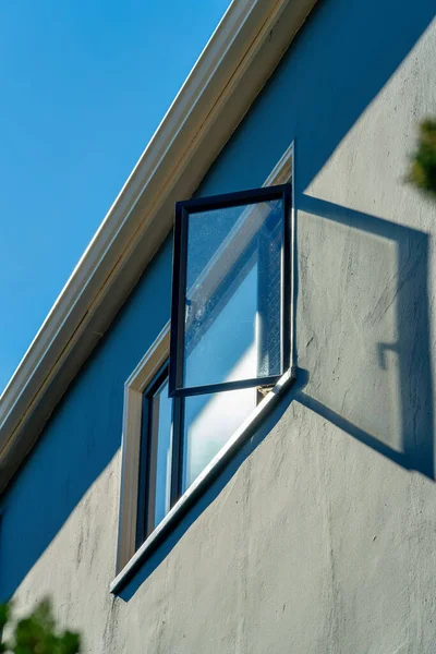 Lone open window on side of urban building or private residence in a downtown neighborhood on house or home. In late afternoon sun with clear blue sky and gray green stucco exterior wall.