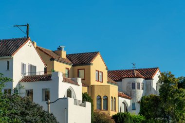 Row of modern houses in the historic districts of downtown san francisco california with front yard trees and blue sky. In late afternoon sun with visible power line pole and balconies.
