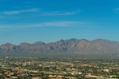 Downtown Tuscon Arizona in the southwest United States and North America with moutains in background and clear blue sky. Visible sky scrapers and houses or homes with businesses in metropolis city.