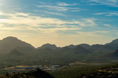 Rocky moutains in the hills of Arizona in the sonora desert at sunset with whispy clouds and silhouette hills. Visible houses and cactuses in the rolling moutains of Tuscon in north american.