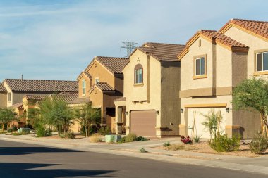 Row of modern suburban houses in a desert region in southwestern north america in Arizona with visible trees. In suburban neighborhood in sun with whispy sky and adobe colors.