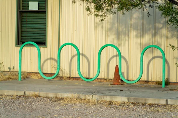 Green bendy bike rack where people can lock their bicycle for security and saftey near a non descript beige building. In a park or urban area to secure your property for green transport in city.